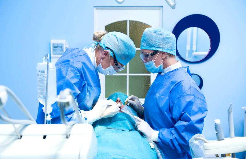 an oral surgeon and an assistant dentist perform a tooth extraction.